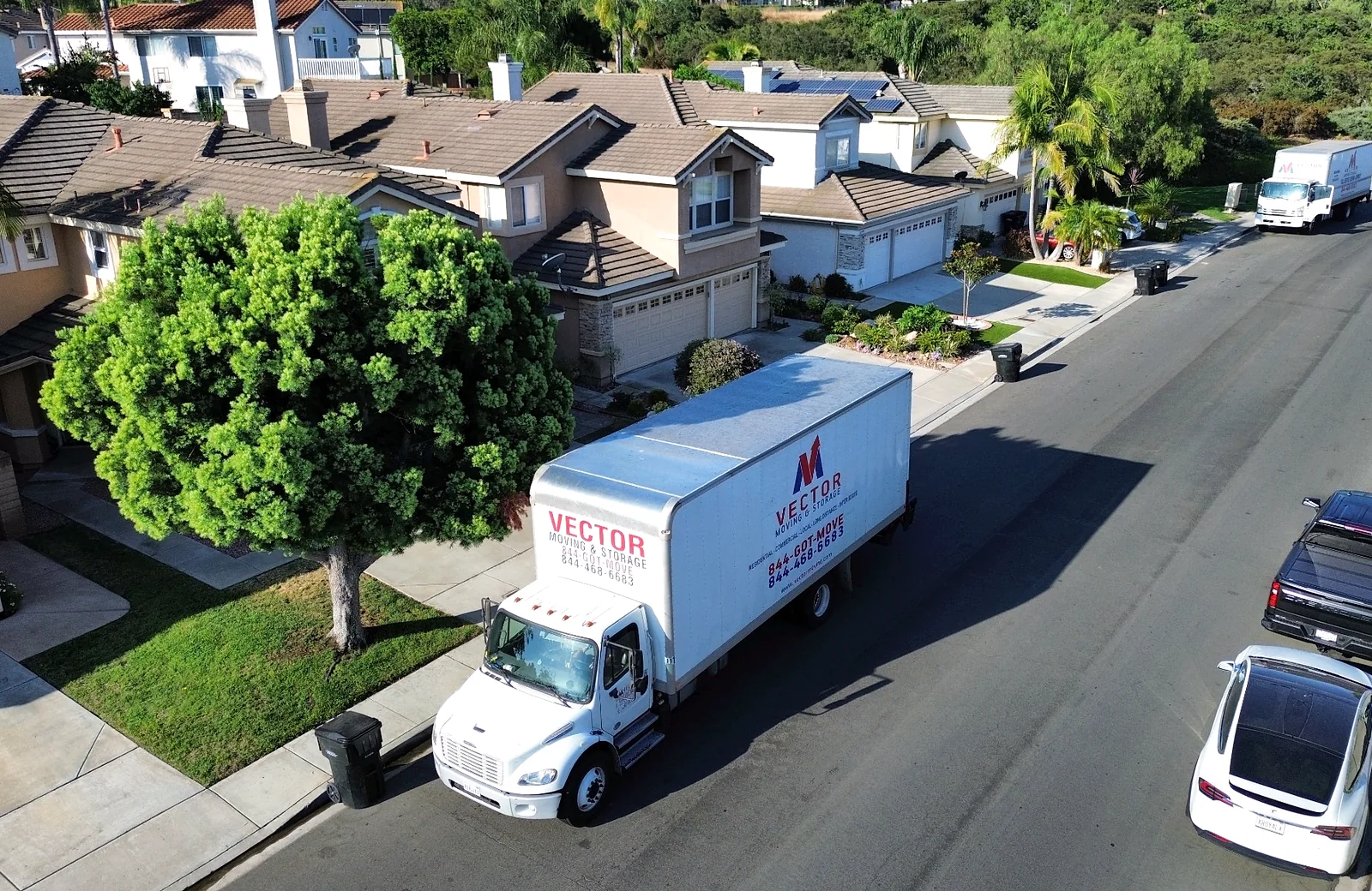 Two branded Vector moving trucks on a residential street