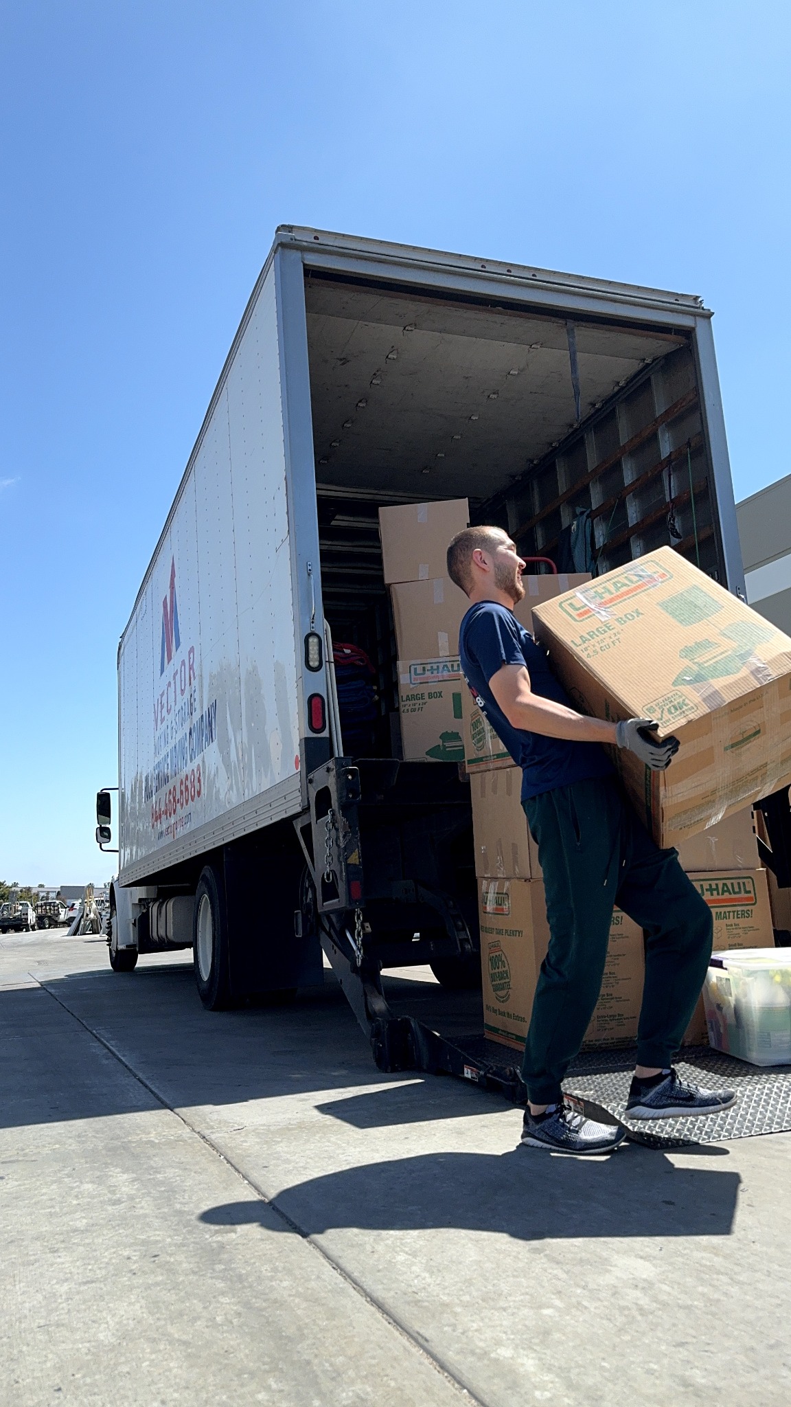 Vector mover carrying cardboard moving boxes beside a moving truck in San Diego