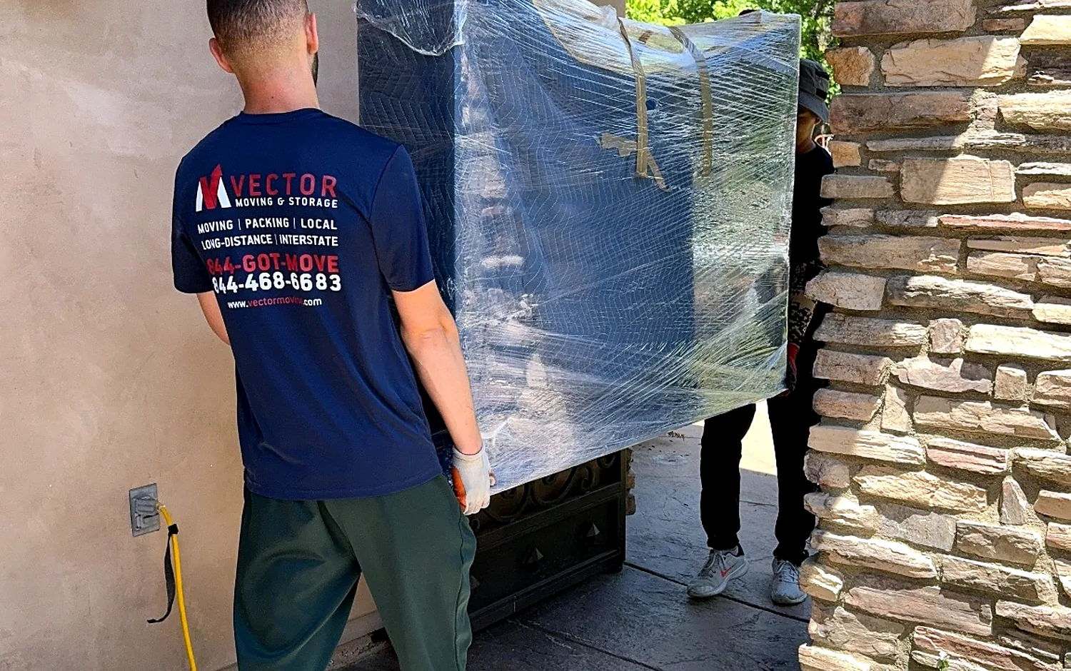 Vector movers guiding a large wrapped furniture piece through a narrow stone entry
