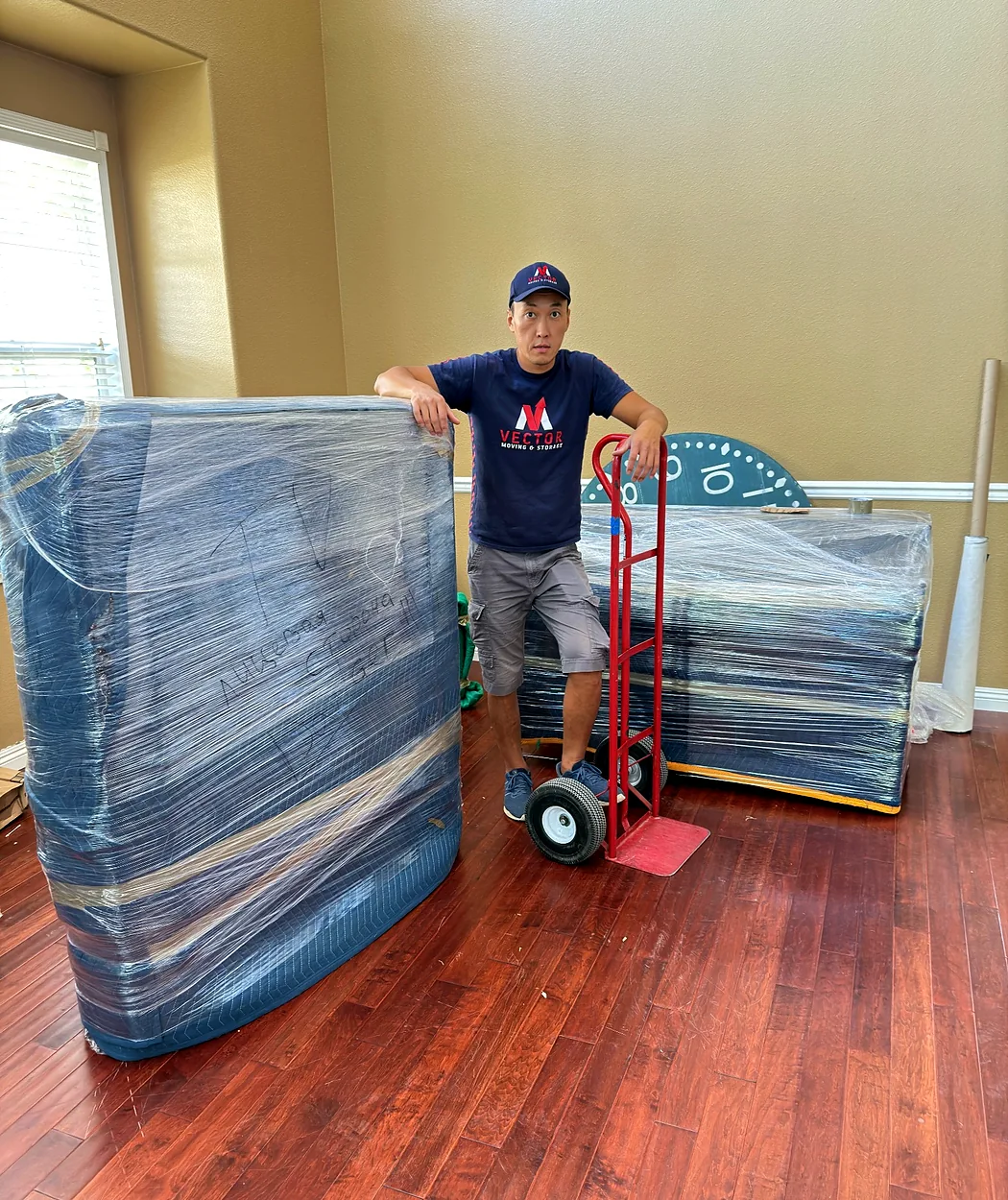 Vector mover standing beside wrapped furniture and a hand truck