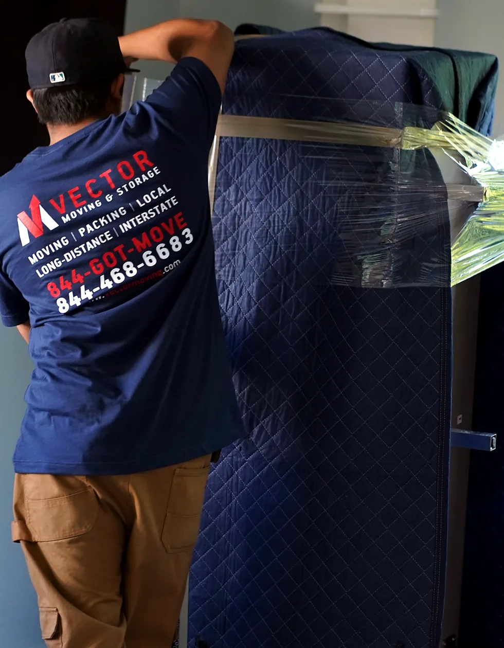 Vector mover wrapping a tall household item with a moving blanket and stretch wrap