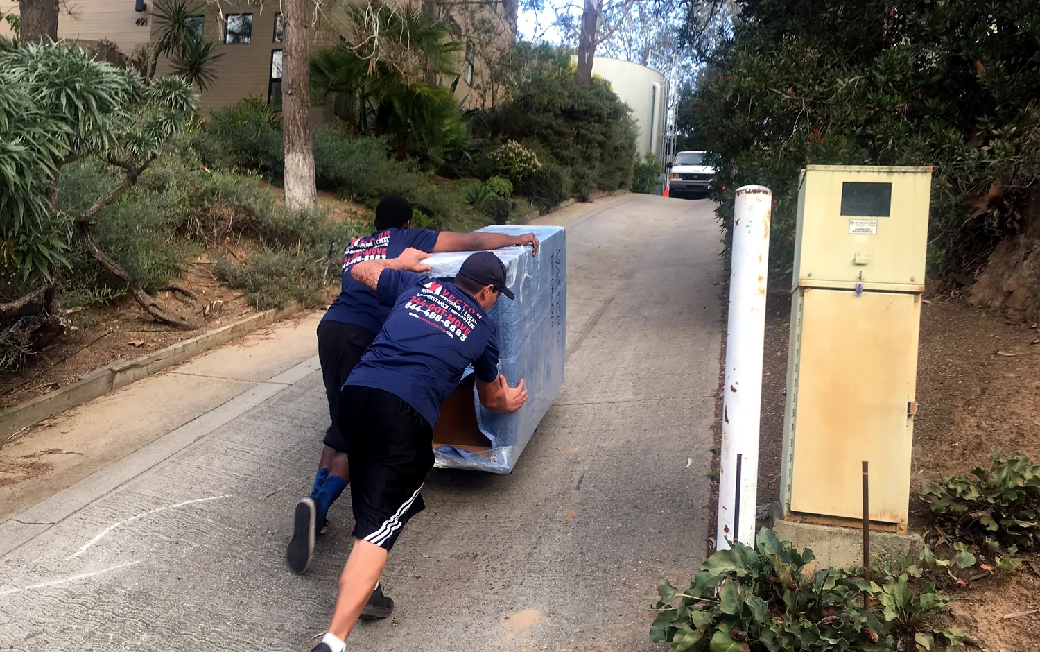 Vector movers controlling a wrapped furniture piece on a steep residential driveway